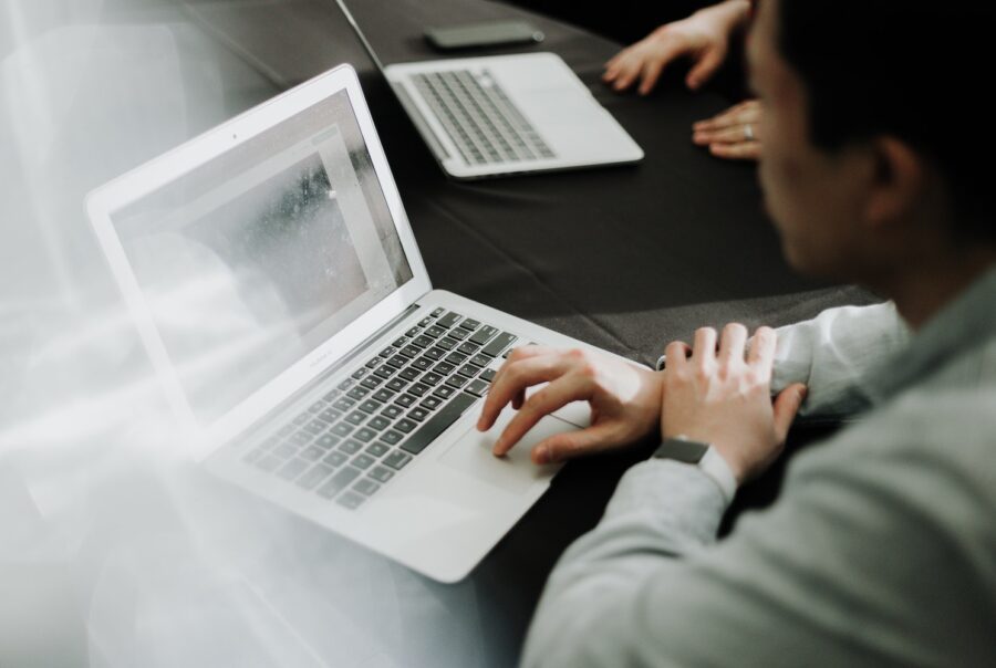 Artistic photo of graphic designer working on MacBook with client blurred in background – behind-the-scenes look at creative process by Shrewsbury-based brand and web designer.