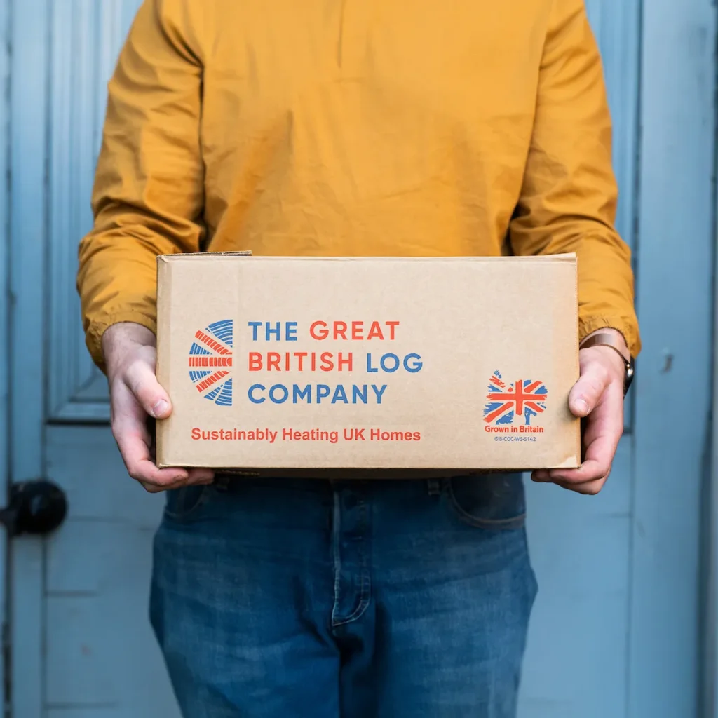 Printed logo on firewood delivery box held by a person wearing vibrant clothes – branded packaging design for Shropshire-based log business. Cropped square.