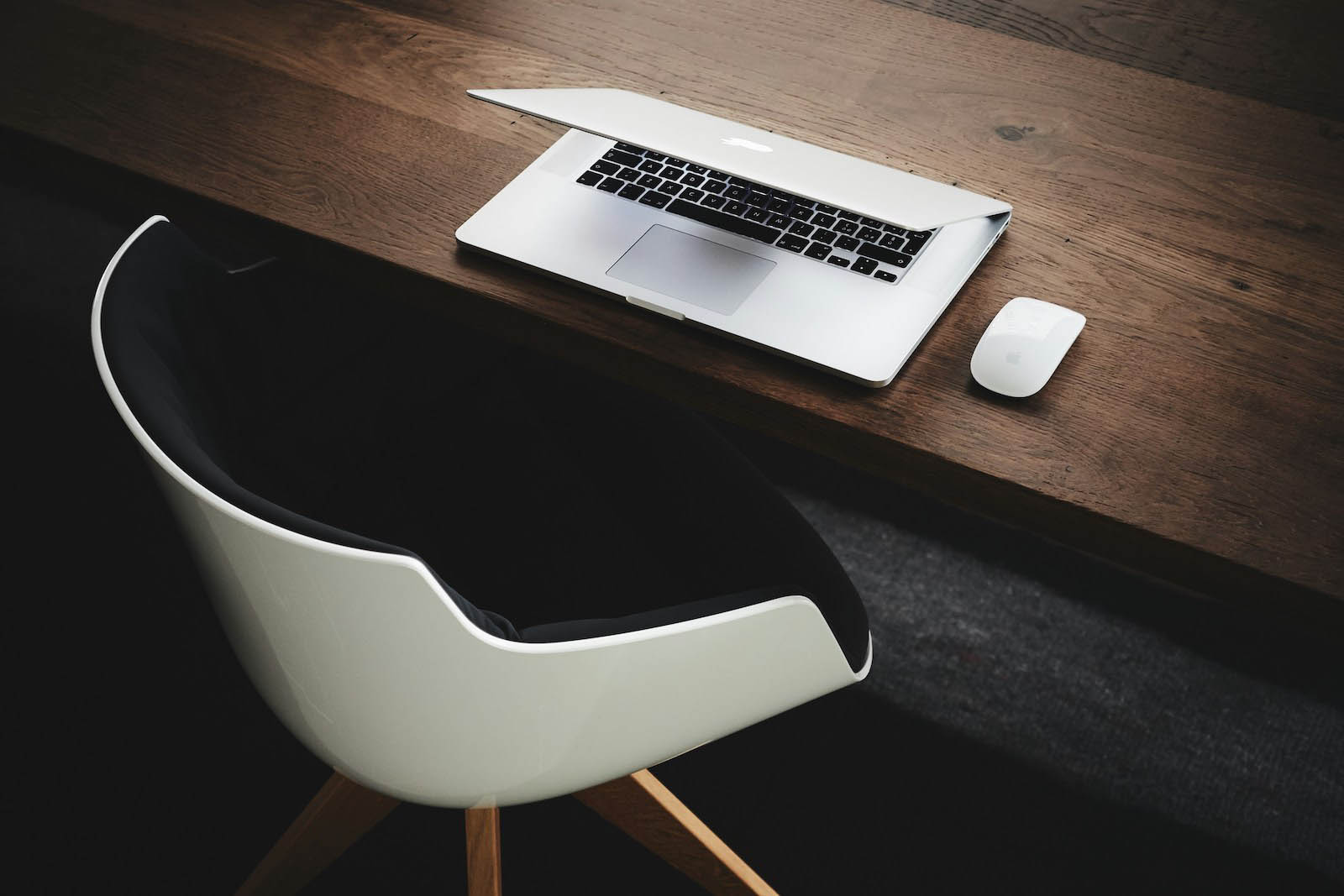 Modern chair at dark desk with MacBook – clean, aspirational workspace visual supporting the importance of professional web design investment.