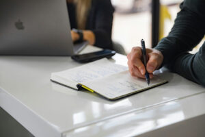 Graphic designer in Shrewsbury taking notes with a client while working on a MacBook.