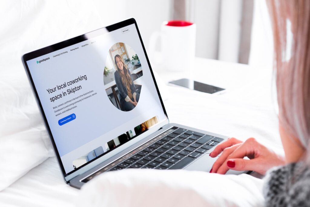 Coworking space website homepage hero on MacBook, designed by a Shrewsbury website designer, woman using laptop on bed. Landscape crop.