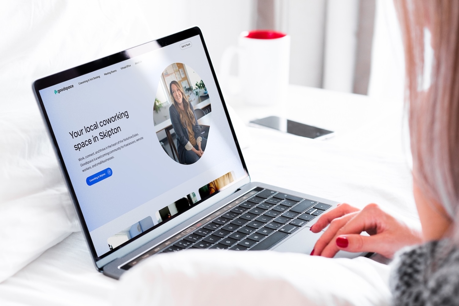 Coworking space website homepage hero on MacBook, designed by a Shrewsbury website designer, woman using laptop on bed. Landscape crop.