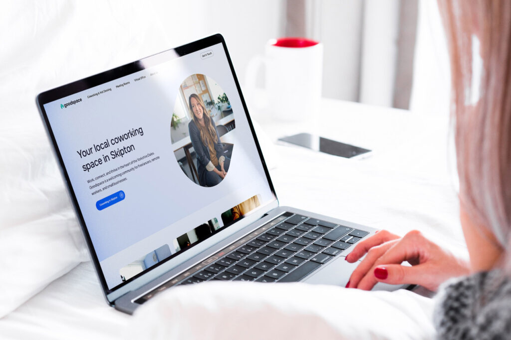 Coworking space website homepage hero on MacBook, designed by a Shrewsbury website designer, woman using laptop on bed. Landscape crop.