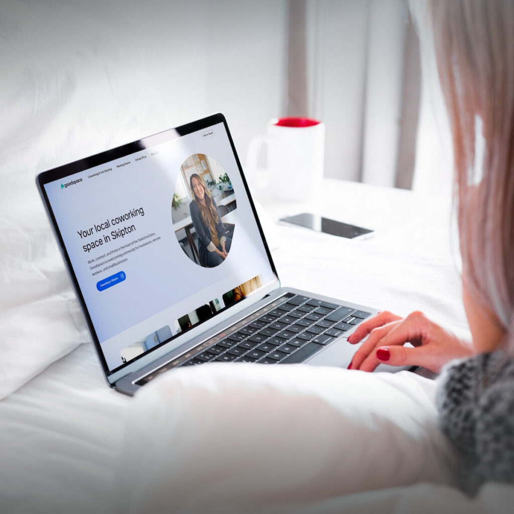 Coworking space website homepage hero on MacBook, designed by a Shrewsbury website designer, woman using laptop on bed. Slim crop.