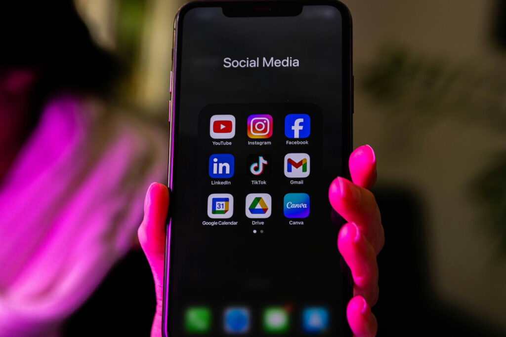 iPhone held up showing social media apps and Canva interface, illustrating DIY design tools